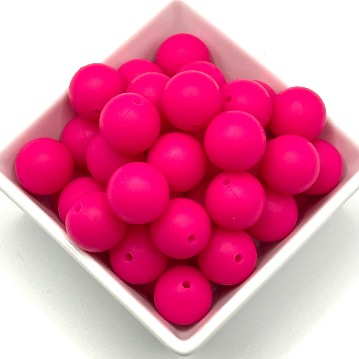 Bright pink silicone round beads with a small hole, displayed in a white square bowl on a white background.
