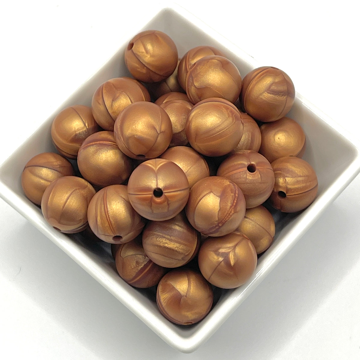 A pile of metallic bronze-colored wooden beads with a central hole, displayed in a white square bowl on a white background.